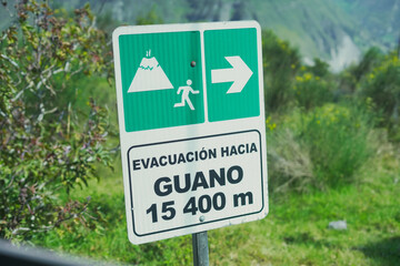 Green and white sign indicating a volcano evacuation route, featuring a volcano icon, a running person