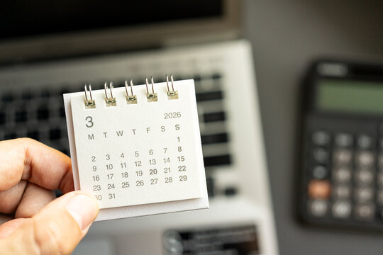 Hand Holding Desk Calendar with Calculator and Laptop for Business Planning in MARCH 2026. calendar MAR 2026. Business planning, finance, accounting, deadlines, and scheduling.
