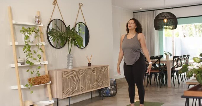 Starting with arms overhead, woman is lowering arms, bending forward on mat at home for stretch