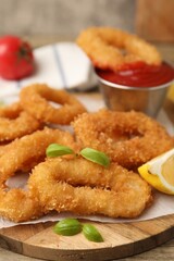 Deep fried squid rings with lemon slice, basil and ketchup on wooden table, closeup