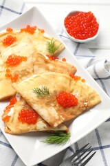 Delicious crepes with red caviar and sour cream on white wooden table, above view
