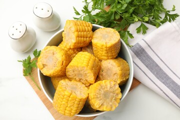 Pieces of tasty corn cobs and parsley on white table, flat lay
