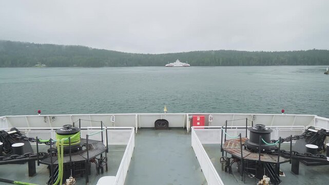 Distant BC Ferry ship in focus with low mountains and clouds under overcast weather. Filmed 7 december 2025. Gulf Islands, British Columbia, Canada
