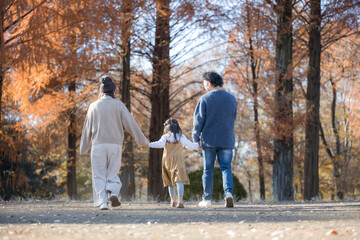 Fototapeta premium 秋の公園で遊ぶ家族 お出かけやレジャーのイメージの手を繋ぐ顔無しの後ろ姿