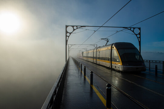 Tram on Luis I bridge emerging from the fog shrouding a church tower in Porto, Portugal