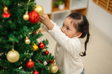 toddler girl decorating toy ball on Christmas tree at home