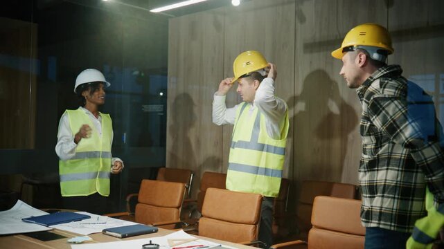 A group of multiracial engineers arrive at the office at the start of the workday wearing safety vests and hard hats.