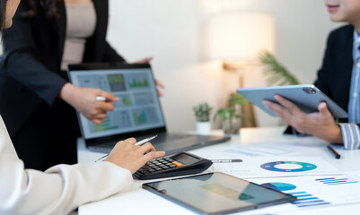 Three business colleagues working together on financial analysis, using digital devices like a laptop and tablet,