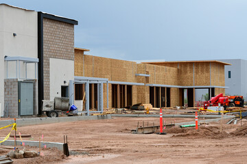 A commercial building under construction with wood framing, concrete block walls, and active site work, illustrating mixed use development and ongoing commercial construction activity