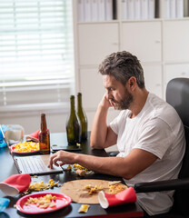 Man having morning hangover. Tired employee work in home office after party. Mature businessman office party mess. Sleepy office worker has hangover. Man at home with laptop. Chaotic morning