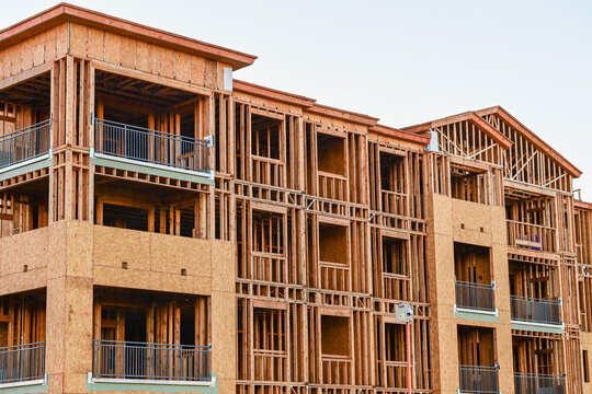 A multifamily apartment building under construction with exposed wood framing and balcony structures, illustrating large scale residential development and structural assembly activity