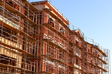 A large multifamily building under construction with extensive scaffolding and exposed wood framing, illustrating major residential development and structural assembly operations