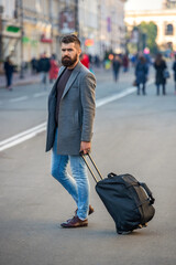 Business trip. Traveling businessman. Bearded tourist traveler walking on city street. Tourist bag city. Bearded stylish man walking and crossing city street with travel bag. Traveler carry luggage