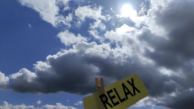 Una nota amarilla con la palabra relajarse en movimiento por el viento sobre un fondo con un cielo con nubes de color blanca y grises un poco desenfocadas