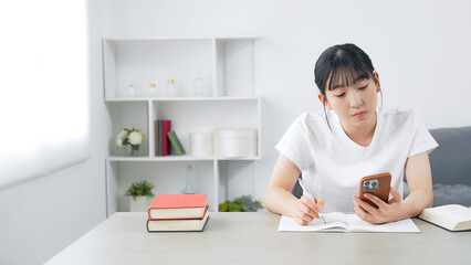 スマホを見ながら勉強する10代女性