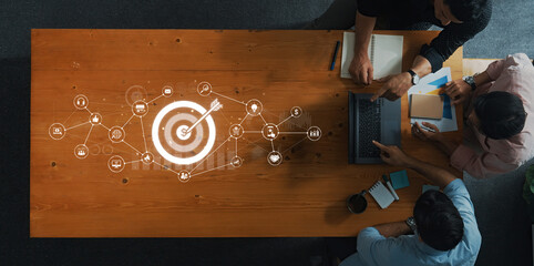 A top view of a group of professionals working on a project strategy, featuring a target symbol and digital icons related to business goals and success. Trope