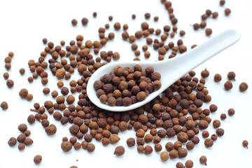 A heap of dark-brown, aromatic allspice berries on a white background.