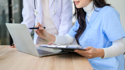 Close up woman doctor holding chart pointing at laptop with senior physician standing at exam table.