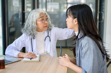 Obraz premium Old asian woman doctor looking or checking on young patient while sitting at table in diagnosis room