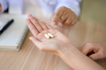 Close up of old doctor pointing explaining medicine pill to young patient at table in diagnosis room
