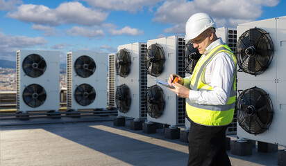 HVAC maintenance technician inspects rooftop cooling units, noting fan performance and system...
