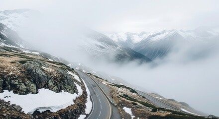 Winding mountain pass road descends through snowy, fog-covered alpine landscape