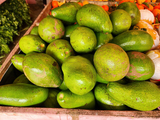 Fresh avocado pile at traditional market stall. Green avocados stacked for retail fruit business. Organic avocado harvest display in local market. Raw avocados for healthy food and grocery sales