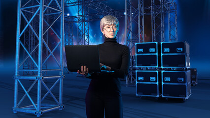 Event production manager oversees digital stage setup using a laptop, coordinating lighting structures and technical equipment for an upcoming performance.
