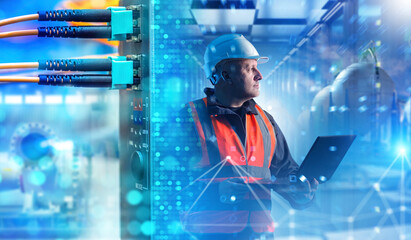 Industrial network technician monitors digital infrastructure with a laptop, inspecting connected...