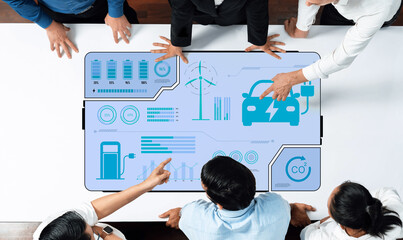 A diverse business team collaborates over an interactive tablet showcasing electric car data and...