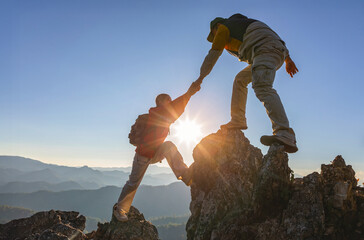 Asia couple hiking help each other.Silhouette Two Male hikers climbing up mountain cliff and one of them giving helping hand. People helping and, team work concept.