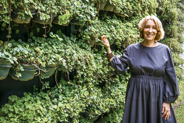 Mature adult woman smiling by green vertical garden