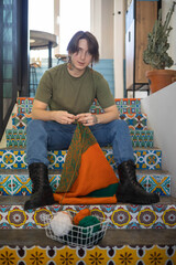 Feminine hipster man crochet handmade use hook knitting needles and wool yarn relaxing on couch