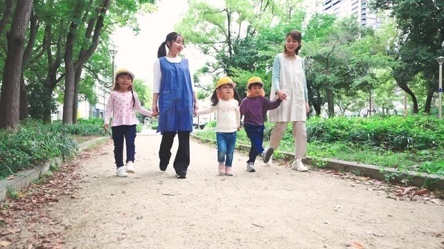 保育士と手を繋いで公園を散歩する園児