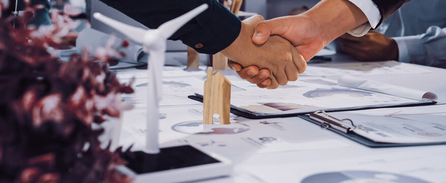 This image captures the moment of a business agreement focused on sustainability, featuring a handshake and green energy models, symbolizing collaboration in eco-friendly practices. SACTR - Powered by Adobe