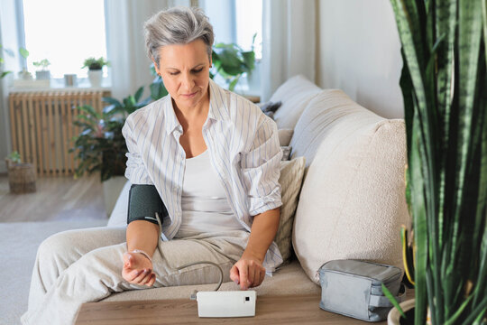 An elderly gray-haired beautiful middle-aged lady measures blood pressure with a tonometer