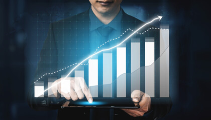 A business professional engages with a digital tablet, analyzing finance data trends against a backdrop of rising graphs and charts, symbolizing growth. Impute