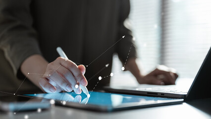 A close-up view of a person analyzing business data on a digital tablet with a stylus, featuring a rising growth chart overlay. Represents business analytics, financial growth, digital strategy.