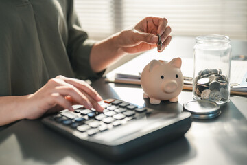 budget, planner, savings, piggybank, finance, goals, A person calculates expenses while placing coins into a piggy bank, symbolizing budgeting, savings, and personal financial planning.