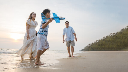 A happy family playing with a toy airplane on the beach during sunset, representing joyful moments, bonding, leisure travel, and the warm, relaxing atmosphere of a summer seaside vacation.