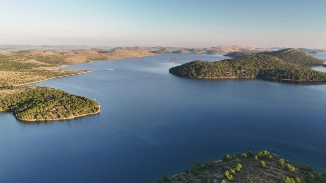 Drone glides over a vast Adriatic bay surrounded by islands and hills, flying towards Kornati in golden sunset light.