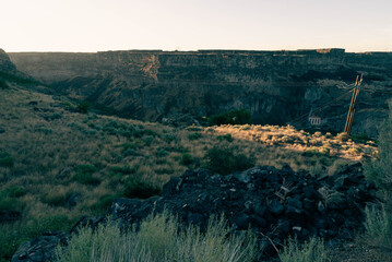 Flat plains dotted with sagebrush and scrub plants extending out to the horizon under a clear blue sky, split in the middle distance by the massive Snake River Canyon just barely visible, in shadow.