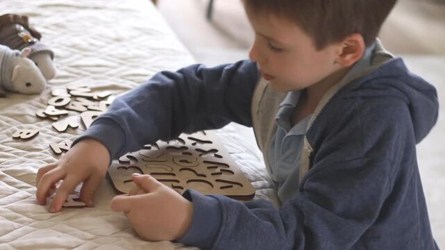 A small preschool boy diligently assembles a wooden puzzle with the English alphabet. The child studies the letters.