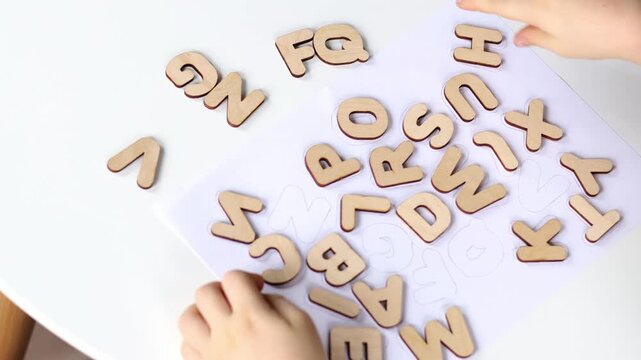 A small preschool boy diligently assembles a wooden puzzle with the English alphabet. The child studies the letters.
