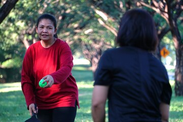 A woman in a red shirt is holding a green ball ready to throw or serve during a pickleball game.