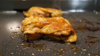 Cooking chicken thighs on a grill in a kitchen at night with lights on and grease bubbling