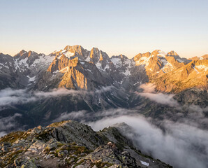 Golden hour light on majestic mountain peaks, valley fog, high alpine view