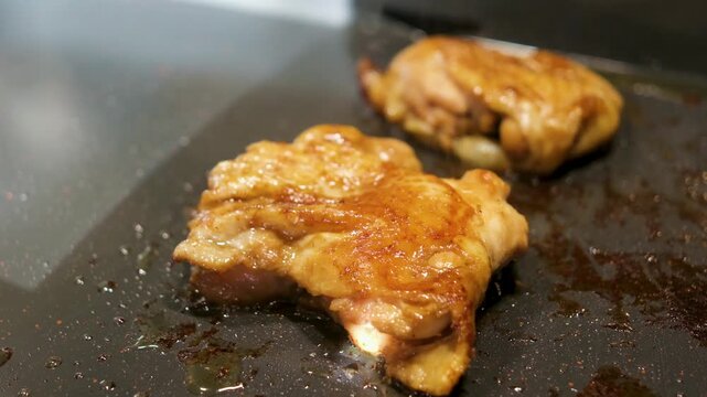Cooking chicken thighs on a grill in a kitchen at night with lights on and grease bubbling - Powered by Adobe