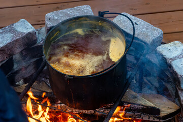 Cast iron cauldron with bubbling stew over wood fire in equipped camping area