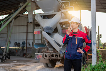 Asian chief engineer standing in cement mixing plant. Background is industrial factory with big cement mixer truck. Material production process and quality control.